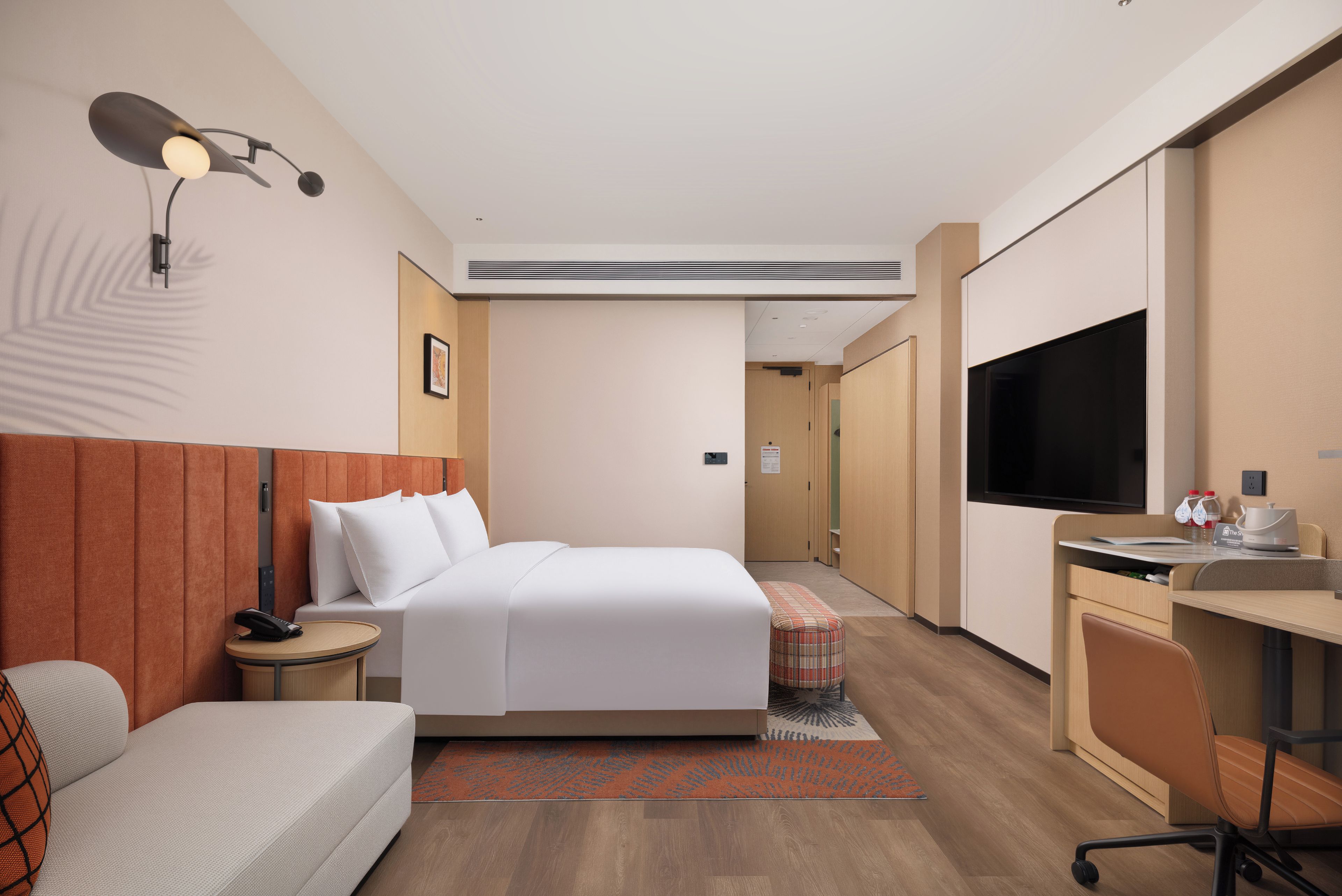 Une chambre d’hôtel comprenant un lit, une table de chevet, une lampe, un bureau, une chaise et un téléviseur.