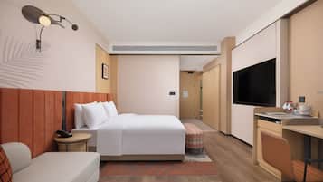 Une chambre d’hôtel comprenant un lit, une table de chevet, une lampe, un bureau, une chaise et un téléviseur.