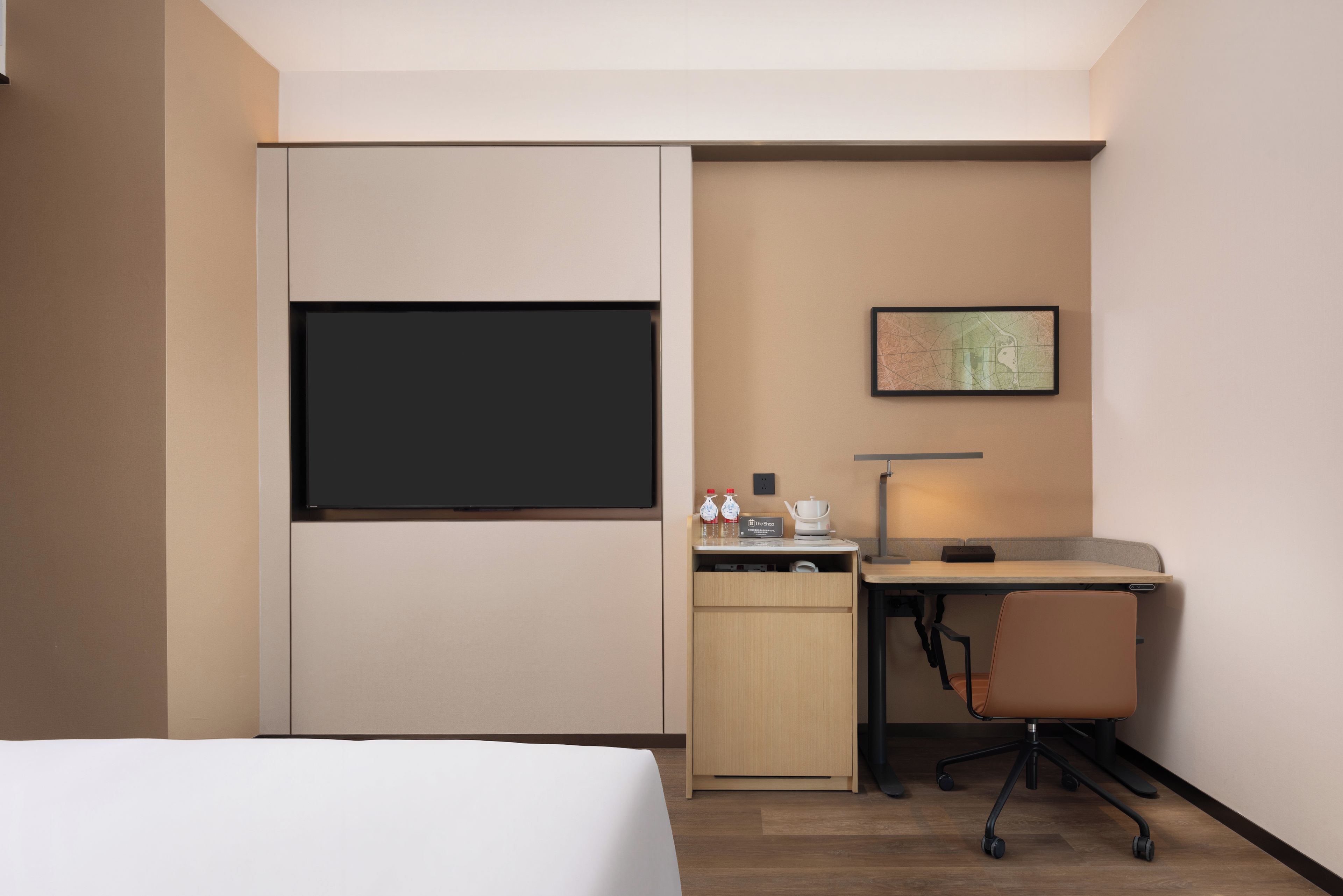 A hotel room with a bed, a desk, a chair, a TV, a coffee maker, and a framed map on the wall.