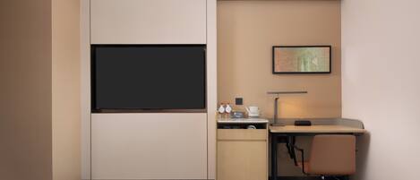 A hotel room with a bed, a desk, a chair, a TV, a coffee maker, and a framed map on the wall.