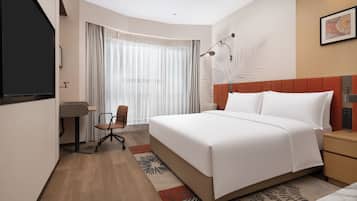 A hotel room with a bed, a desk, a chair, a TV, and a window with curtains.