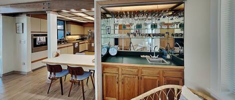 A modern kitchen with wooden cabinets, a dining area with chairs, and a built-in glass display for kitchenware.
