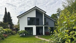 A modern two-story house with a balcony, surrounded by lush greenery and a clear sky. - Haus an der Panke, room with bathroom (Panketal)