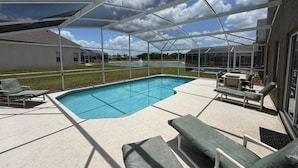 A covered outdoor pool area with lounge chairs and a table, surrounded by a glass enclosure. - Lakeview Villa (Davenport)