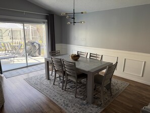 Ein Essbereich mit Tisch, Stühlen, einer Deckenleuchte und Blick durch eine Glastür.