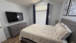 A bedroom with a bed, a dresser, a television, and a window with curtains. - Beach Bums Villa (Davenport)