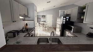 A modern kitchen with white cabinets, a stainless steel refrigerator, and a dining area with a table and chairs. - Beach Bums Villa (Davenport)