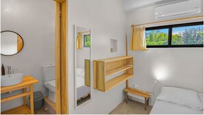 A modern bathroom with a wooden vanity, a toilet, a mirror, and a window with a view of greenery. - Jungle Studio -Steps to Beach-Wi Fi -AC-Work-Surf (Santa Teresa)
