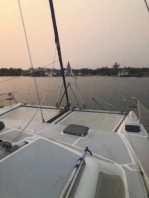 A boat's deck with a netted area, a small cabin, and a view of the water and distant buildings.