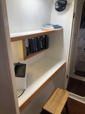 A small room with a desk, a shelf with binders, a pair of headphones, and a small stool.