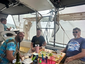A boat interior with a dining table, chairs, and a person seated. - FREE snorkel trip with 2 night stay. Starlink, 3 Queen Bd, On the water. (Bocas del Toro)
