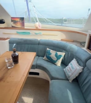 A boat interior with a wooden table, a cushioned seating area, and a window with a view of the water.