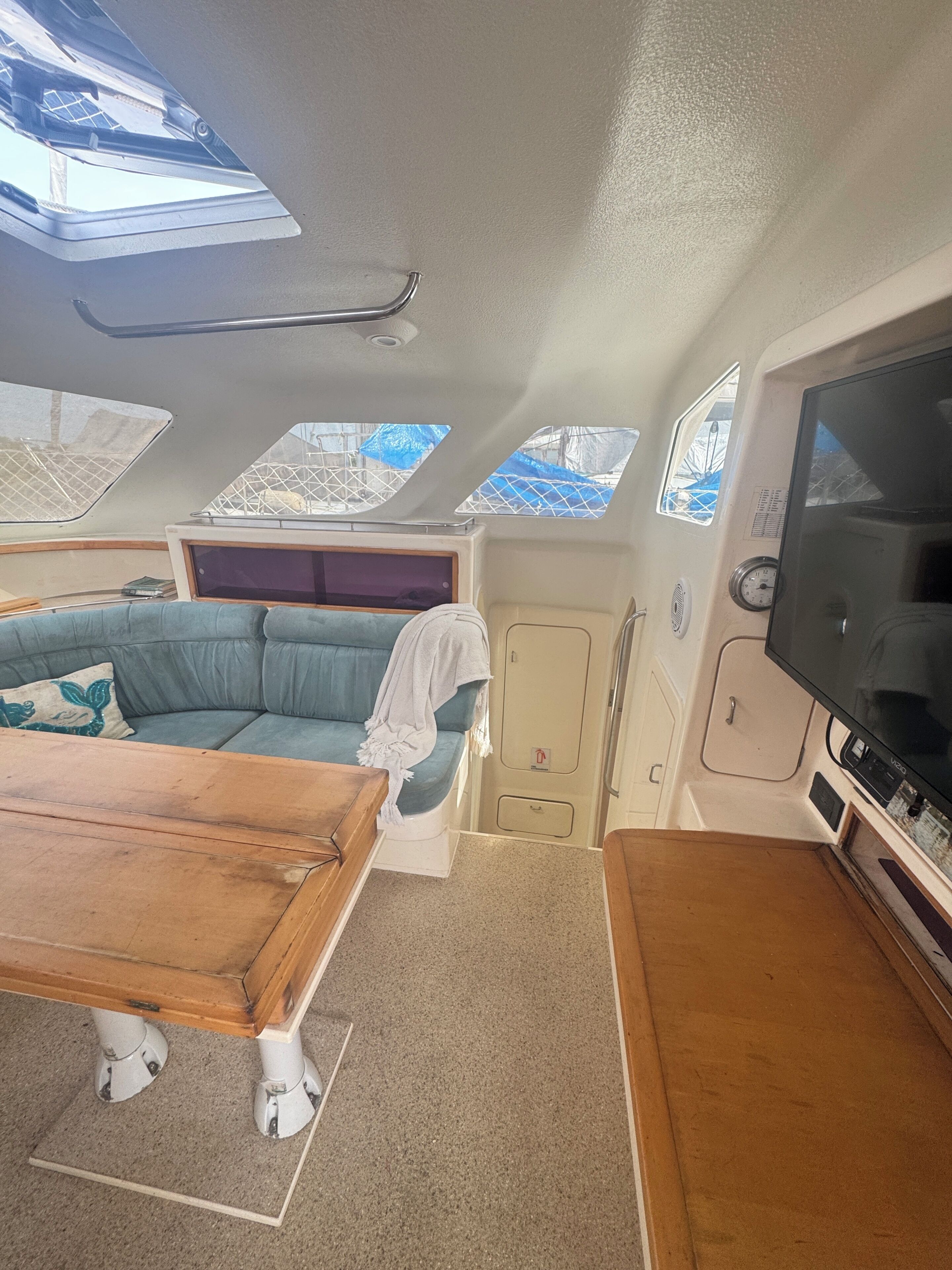 Interior de barco con sofá, una mesa, televisor y tragaluces.