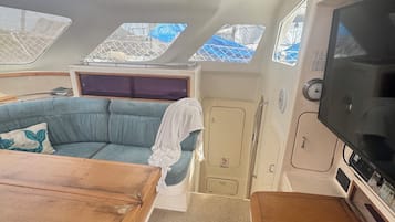 Interior de barco con sofá, una mesa, televisor y tragaluces.