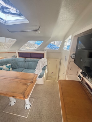 A boat interior with a sofa, a table, a television, and skylights.
