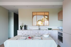 A modern kitchen with a dining table set for four, a coffee machine, and a large window with a view. - Chiberta - Ocean and Golf Suite - Pool - Beach (Anglet)
