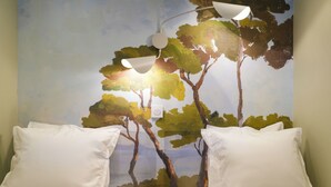 Un dormitorio con dos camas, almohadas blancas, un mural de árboles y una lámpara en el techo.
