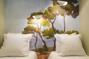A bedroom with two beds, white pillows, a mural of trees, and a ceiling light fixture. - Chiberta - Ocean and Golf Suite - Pool - Beach (Anglet)