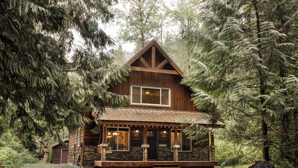 Eine rustikale Holzhütte mit Steinunterbau, Holzfassade und einer Veranda mit Beleuchtung.