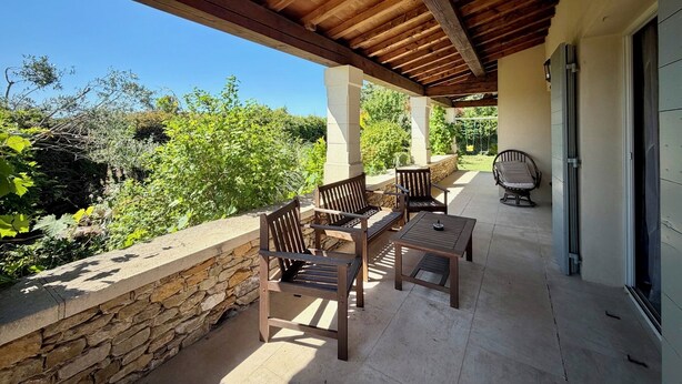 A covered patio with stone walls, wooden furniture, and a view of greenery. - 3-bedroom family house, swimming pool, garden and terrace near Uzès (Serviers-et-Labaume)