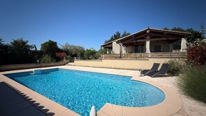 A swimming pool with a stone deck, a covered patio area, and a view of a house with a stone facade. - 3-bedroom family house, swimming pool, garden and terrace near Uzès (Serviers-et-Labaume)