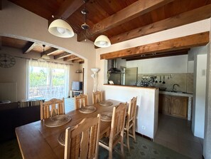Ein Essbereich mit Holztisch und Stühlen, eine Küche im Hintergrund und Blick ins Freie.