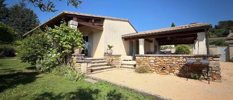 Uma casa com fachada de pedra, alpendre coberto e entrada por um caminho de cascalho.