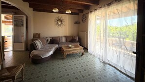 A cozy living room with a wooden ceiling, a sofa, a coffee table, and a large window with sheer curtains. - 3-bedroom family house, swimming pool, garden and terrace near Uzès (Serviers-et-Labaume)