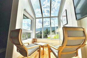 A room with a large skylight, two wooden chairs, a small table, and a view of a house and trees.