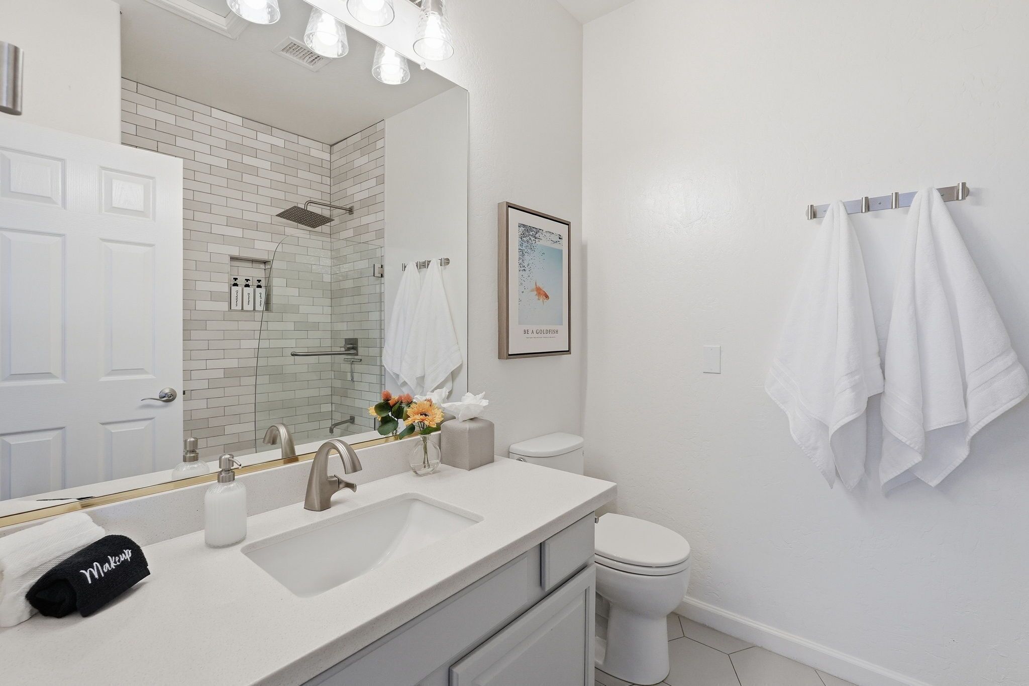 Une salle de bain moderne avec un lavabo, un miroir et des toilettes blancs. On y trouve des serviettes et des articles de toilette sur le comptoir.