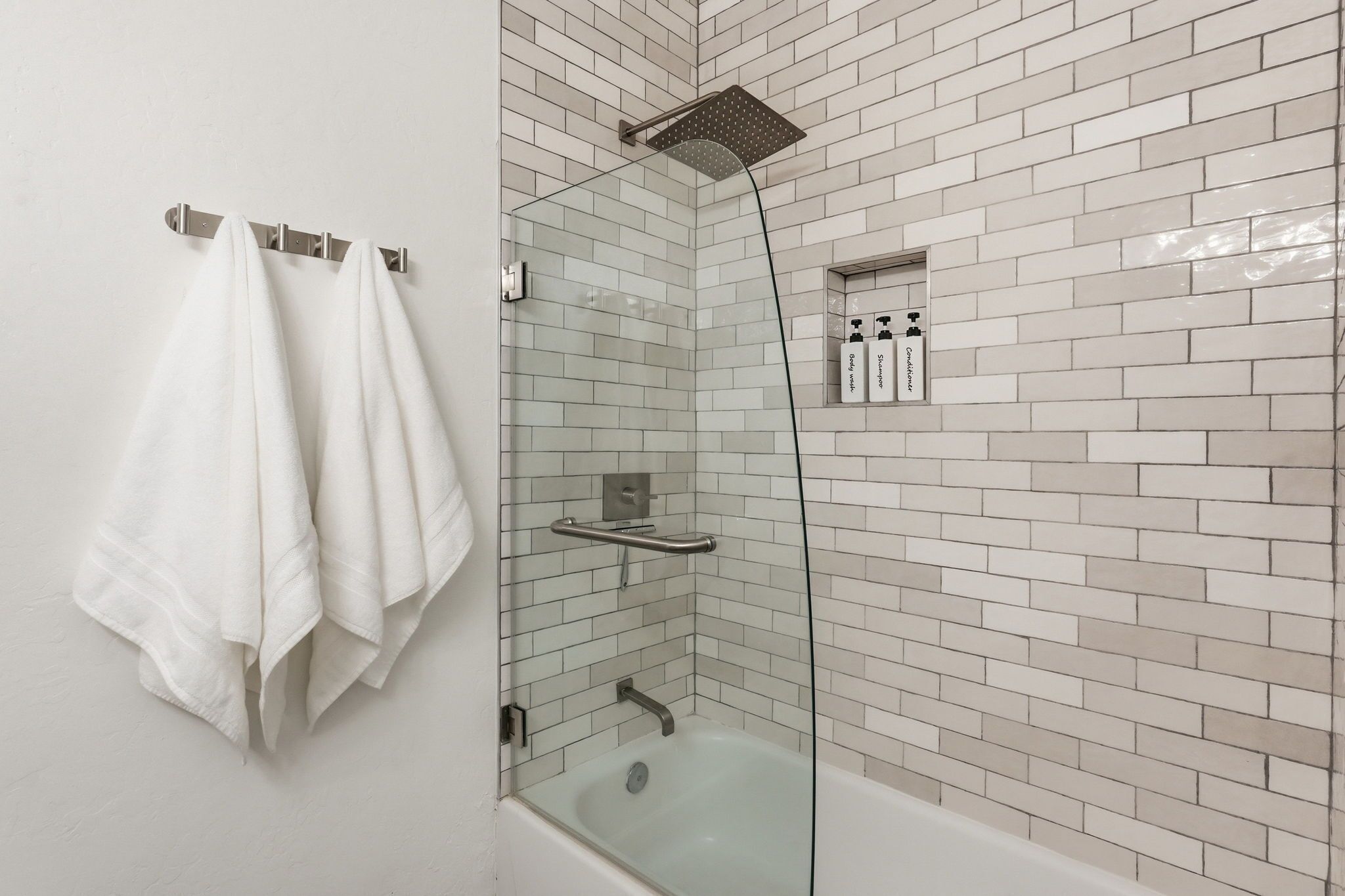 A shower with a glass enclosure, a glass-enclosed bathtub, and a towel rack with towels.