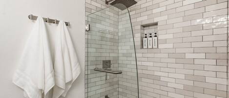 A shower with a glass enclosure, a glass-enclosed bathtub, and a towel rack with towels.