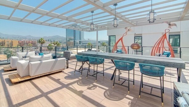 A rooftop terrace with a white sofa, bar stools, and a dining table. - Cozy modern Hollywood Getaway (Beverly Hills)