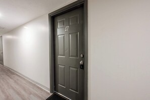 Ein Flur mit einer dunkelgrauen Tür, die mit der Nummer 8 gekennzeichnet ist, einer hellen Wand und einem Holzboden.