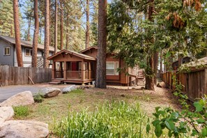 Eine Holzhütte mit Veranda, umgeben von Bäumen und einem Holzzaun.