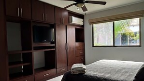 Ein Schlafzimmer mit Bett, Kleiderschrank, Deckenventilator und einem Fenster mit Blick ins Grüne.