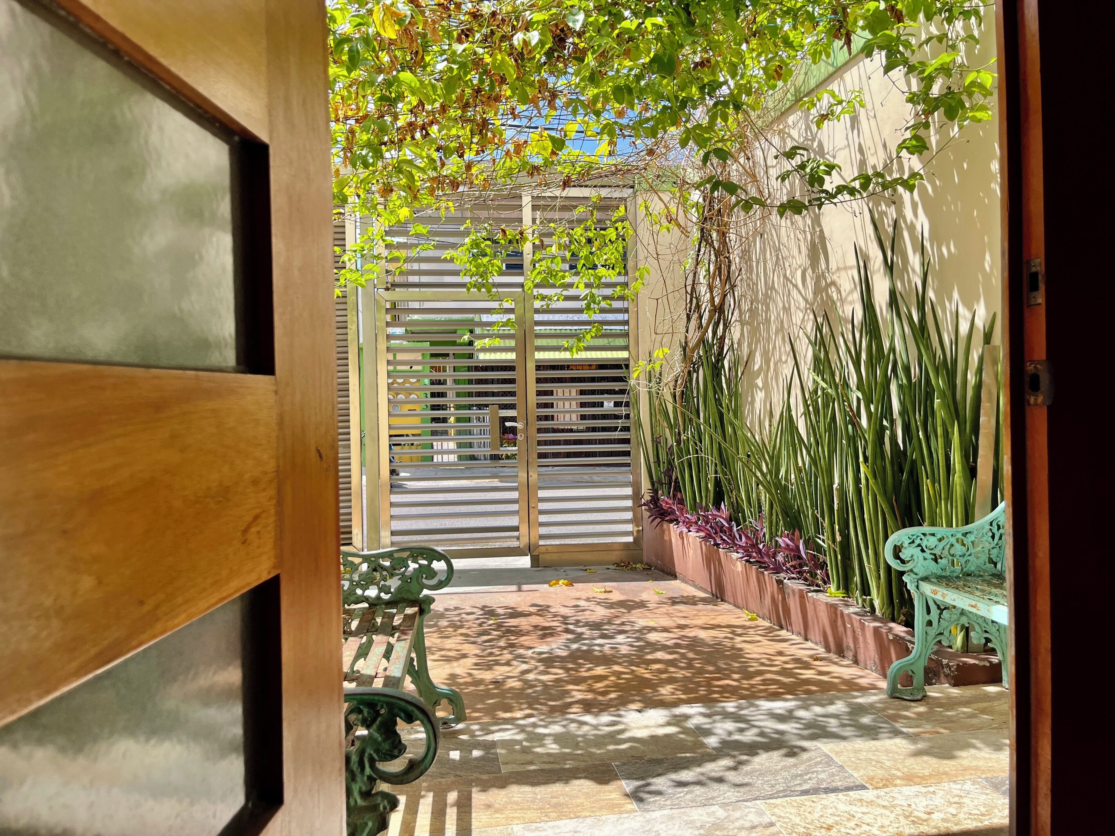 An open doorway leading to a courtyard with a bench, a potted plant, and a metal gate.