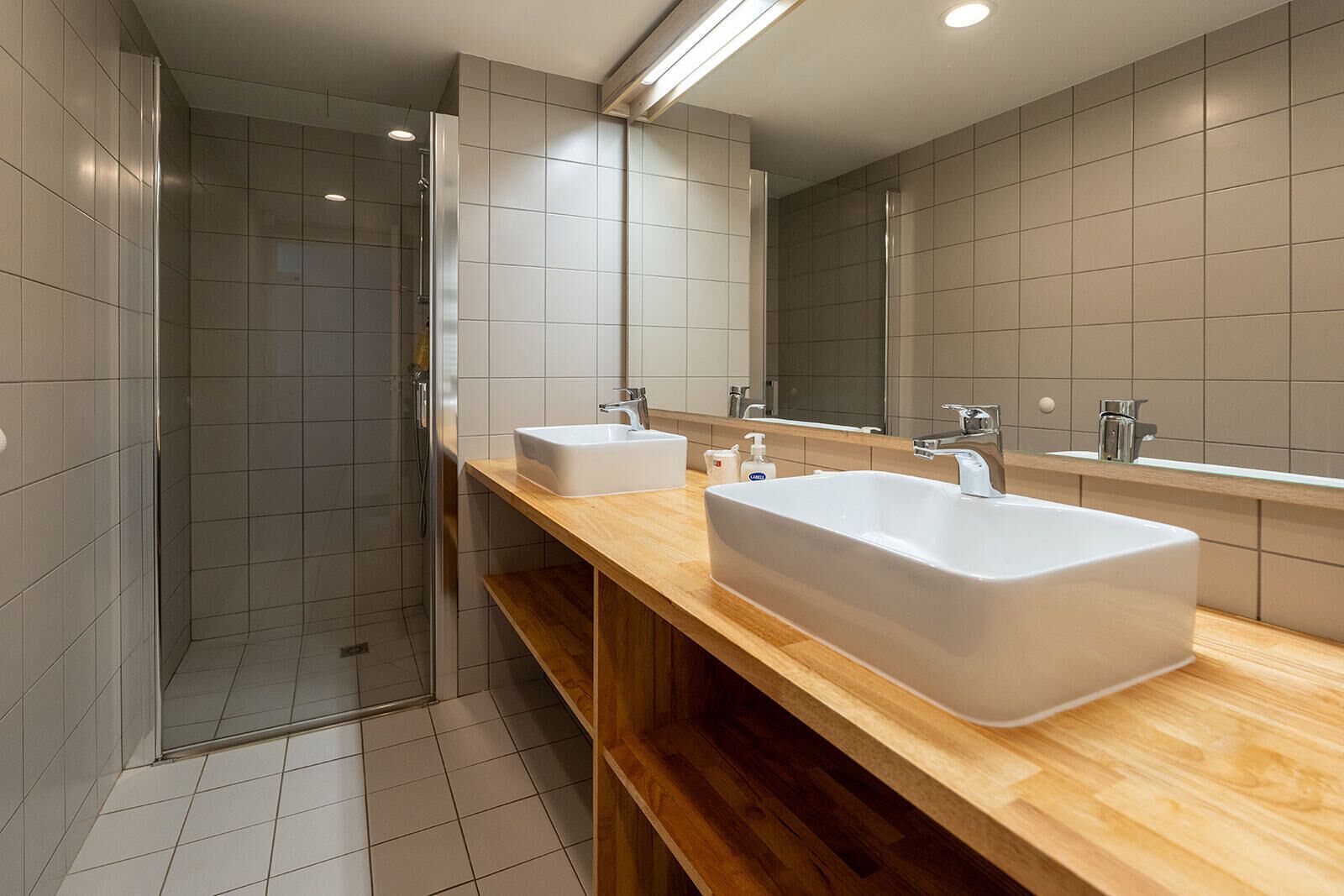 Un bagno moderno con doccia, due lavandini e un grande specchio.