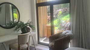 A room with a desk, chair, bed, and a large window with a view of greenery.