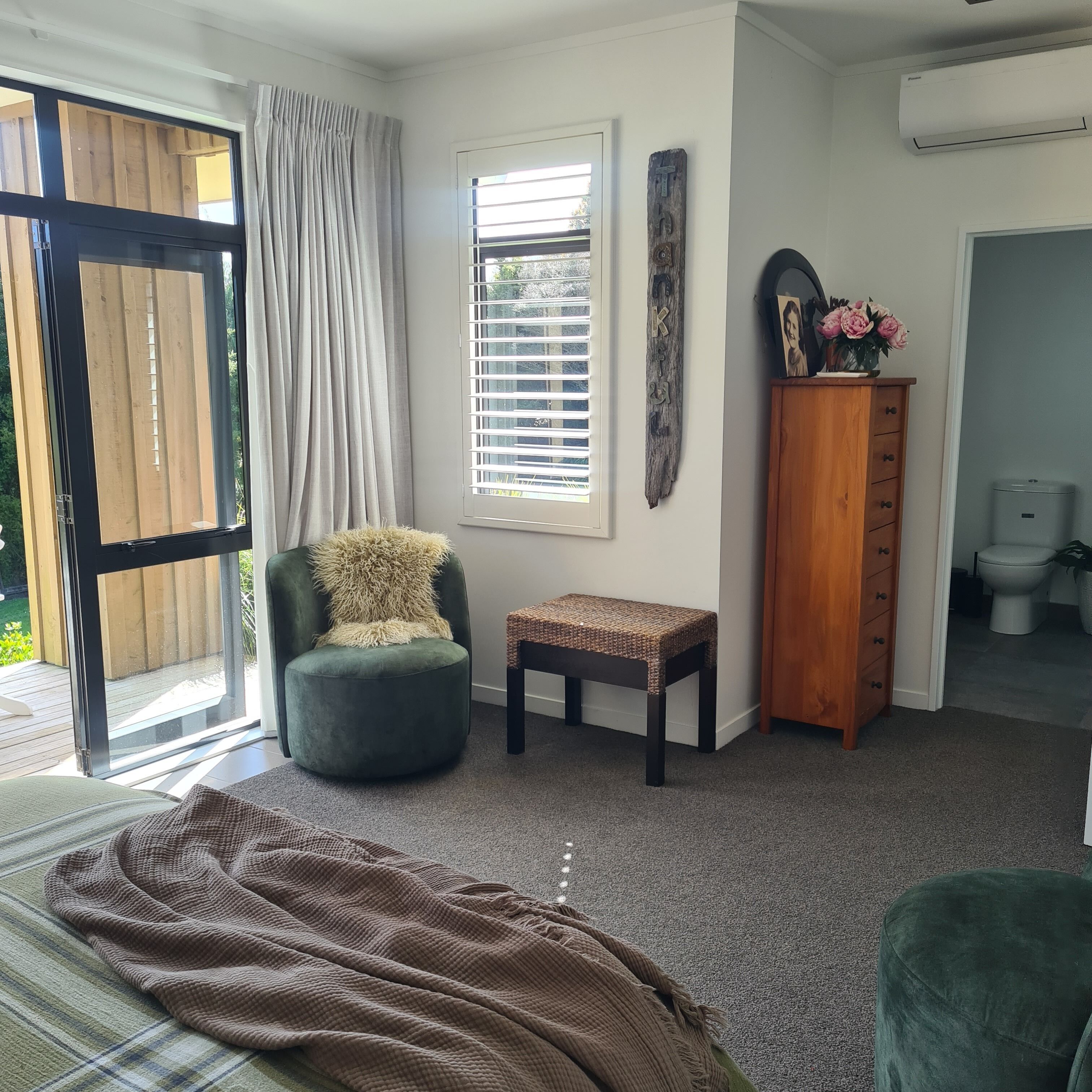 A room with a green chair, a small table, a wooden cabinet, and a large window with blinds.