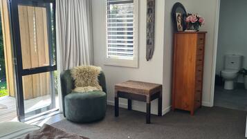 A room with a green chair, a small table, a wooden cabinet, and a large window with blinds.