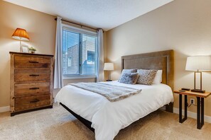 Ein Schlafzimmer mit einem Bett, einem Schminktisch, einem Nachttisch und einem Fenster mit Jalousien.