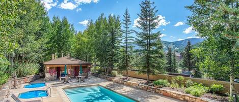 A pool area with lounge chairs, a small gazebo, and a view of mountains.