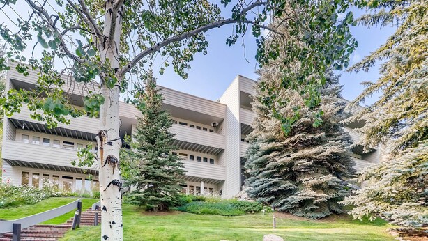 A modern building with a flat roof, surrounded by a well-maintained lawn, large trees, and a staircase leading to the entrance. - Sun Vail 21b, 3BD Condo With Vail Mountain Views (Vail)