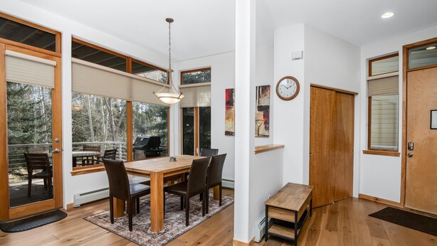 A dining area with a wooden table, chairs, and a rug. There is a bench, a clock on the wall, and a door with a window. - Savoy Villas 4D, 3BD Vail Condo With Garage (Vail)
