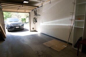Eine Garage mit einem draußen stehenden Auto, einem an der Wand montierten Fahrrad und einer an der Wand angelehnten Leiter.