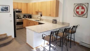 A modern kitchen with wooden cabinets, stainless steel appliances, a marble countertop, and a bar area with stools. - Savoy Villas 4D, 3BD Vail Condo With Garage (Vail)
