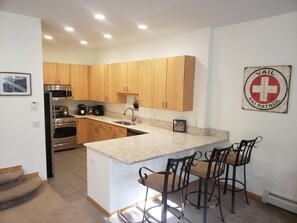 Eine moderne Küche mit Holzschränken, Edelstahlgeräten, einer Marmorarbeitsplatte und einer Bar mit Hockern.