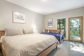 Ein Schlafzimmer mit einem großen Bett, einem kleineren Bett, einem Fenster und einer Tür, die auf einen Balkon führt.