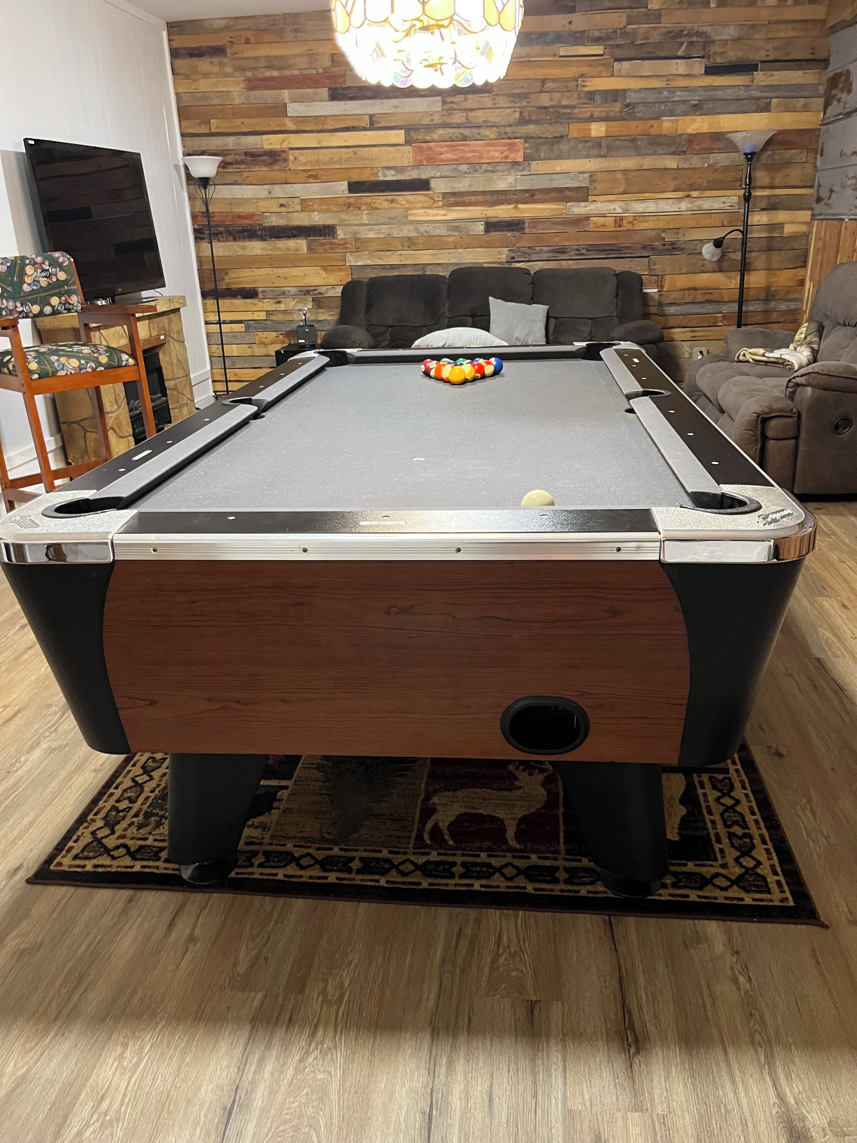 A pool table in a room with a wooden wall and a chandelier.